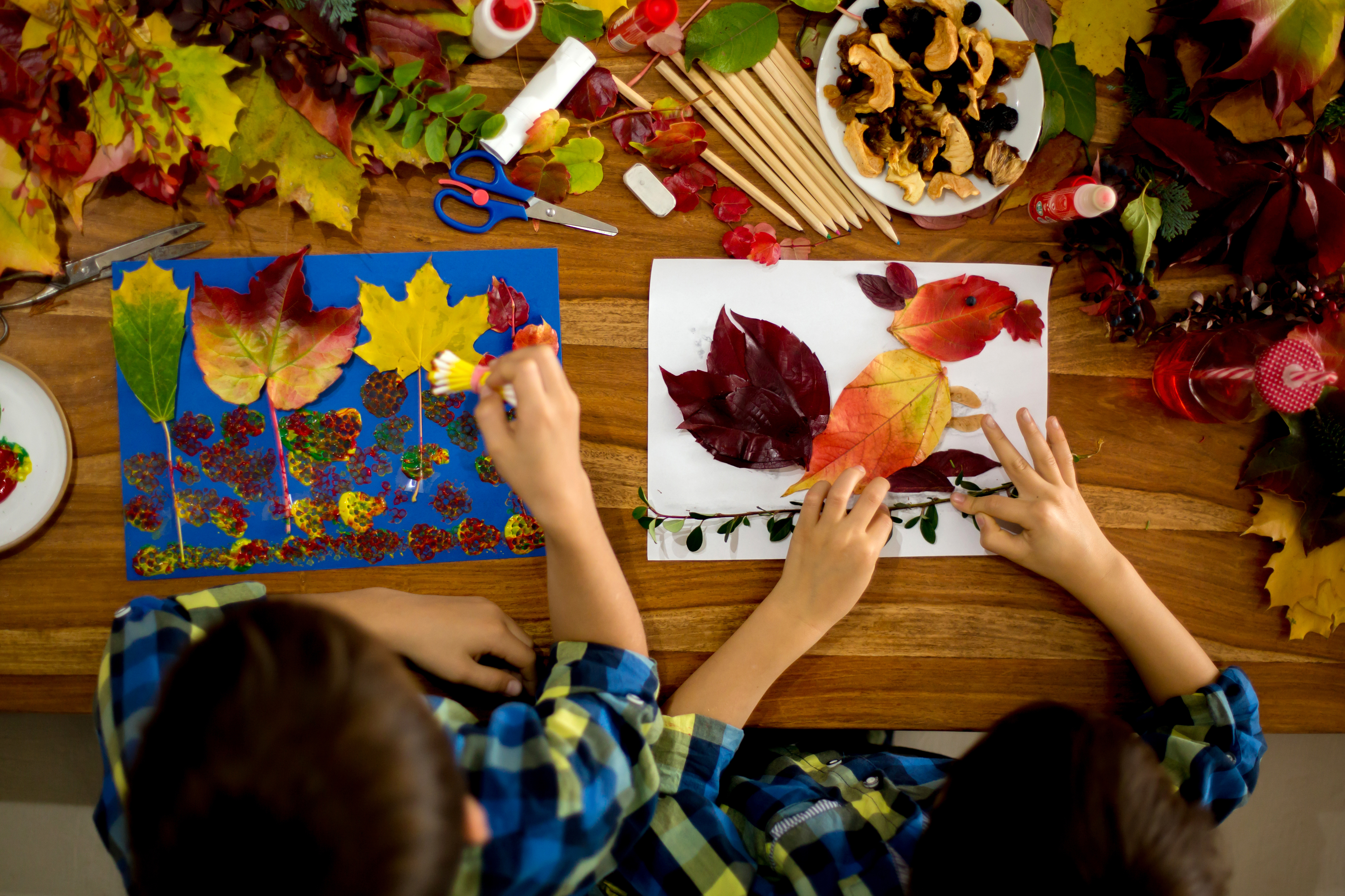 Zwei Kinder sitzen am Tisch und basteln bunte Herbstbilder